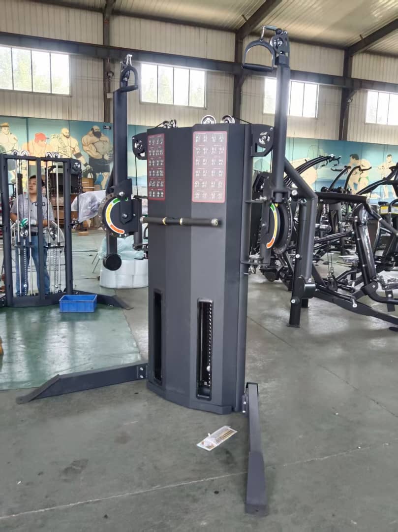 A black multi-station cable machine with twin weight stacks and adjustable pulley towers, photographed on a factory floor.